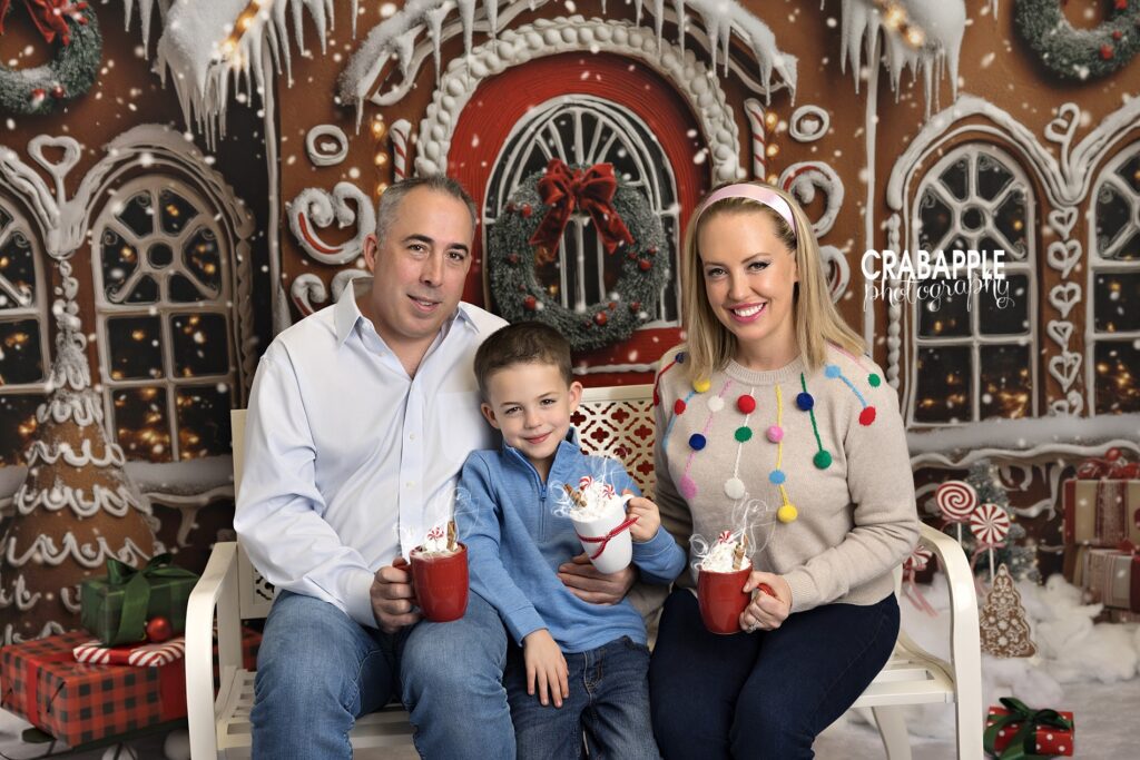 Mom and dad posing with their son while holding hot cocoa in a holiday studio
