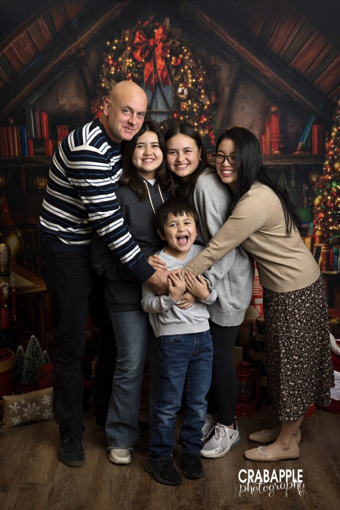 Parents hugging their three children in a joyful holiday studio family portrait
