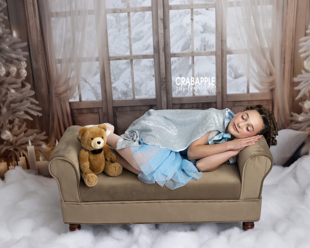 A young girl pretends to sleep on a small couch during holiday dance studio photos