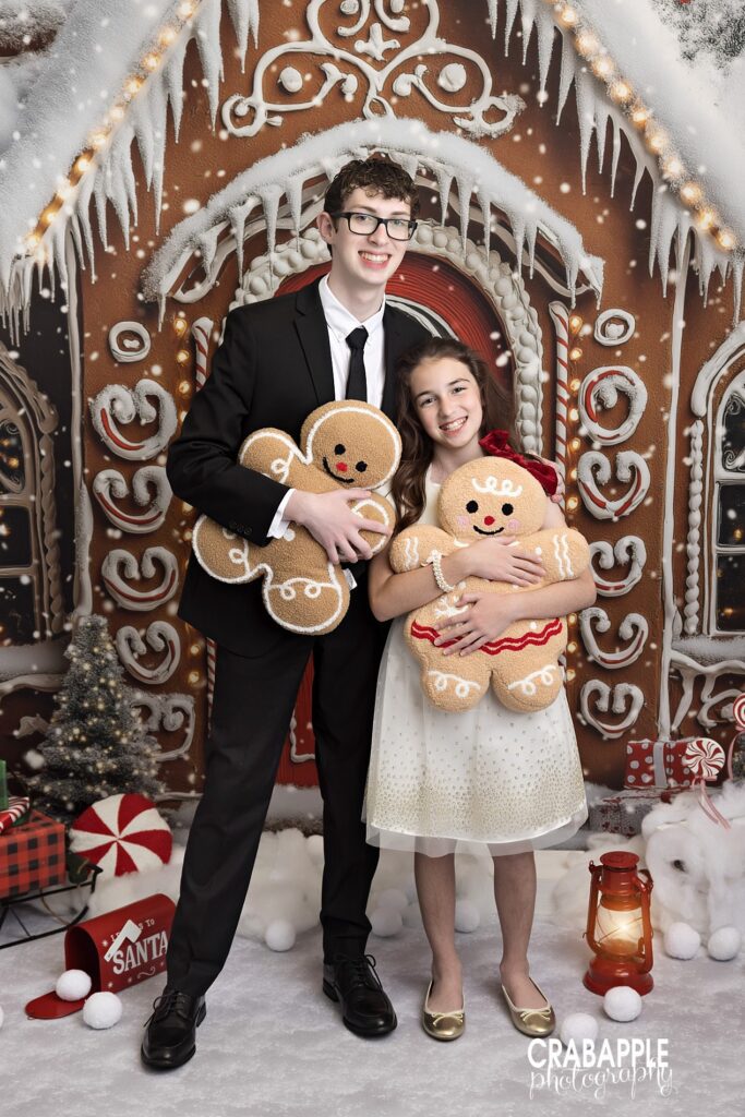 Two siblings in formal outfits holding gingerbread stuffed animals in a holiday portrait
