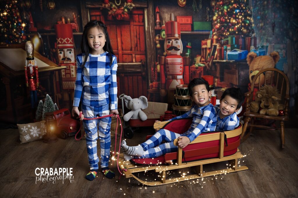 Sister pulling her brothers in a sled during a playful holiday studio portrait
