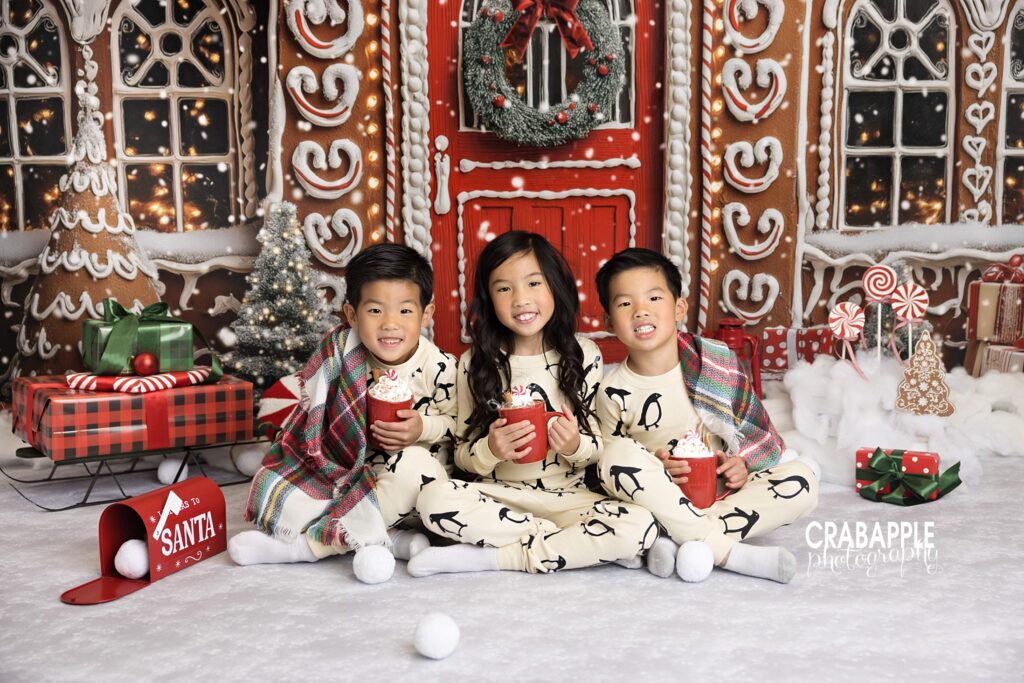 Three siblings in matching Christmas pajamas holding mugs of hot cocoa during holiday portraits.