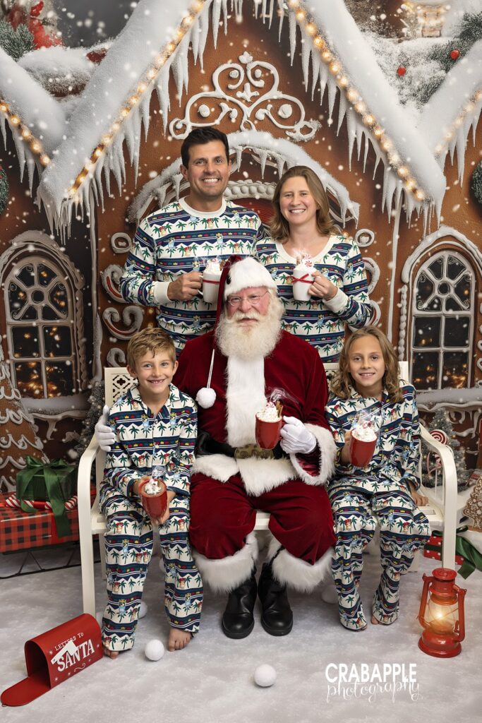 Mom, dad, and two sons all wear matching Christmas pajamas and pose with Santa during holiday mini session near Boston