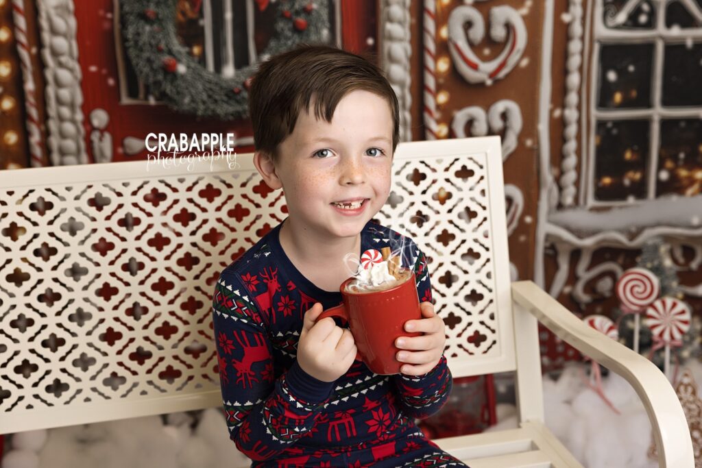 Young boy smiling while holding hot cocoa during a holiday studio session
