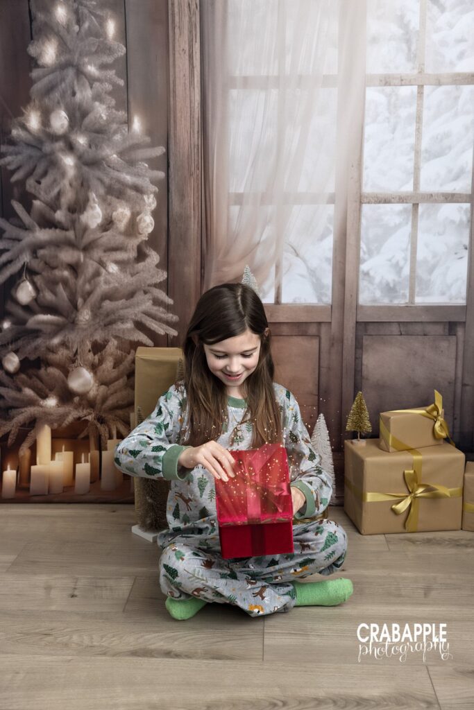 Young girl in pajamas opening a Christmas gift during a studio photo session
