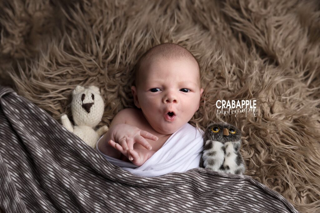 North of Boston newborn photoshoot ideas Awake newborn in a candid portrait with stuffed animals and brown fur during north of Boston newborn photoshoot