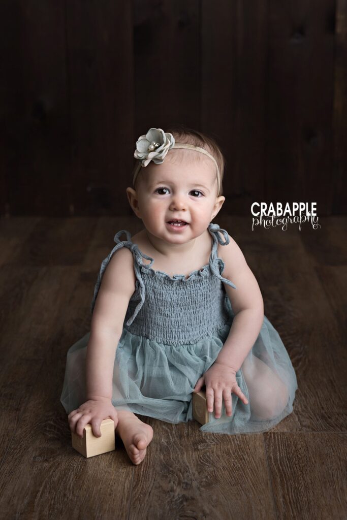 Classic baby pictures in Andover MA studio Natural baby pictures of one-year-old girl sitting on dark wood backdrop in Andover MA studio