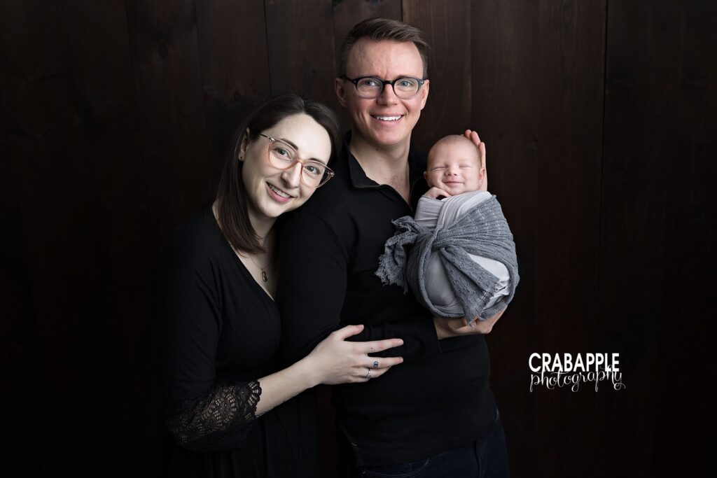 Newborn baby photoshoot with family in Andover MA studio Family posing together during a newborn baby photoshoot in an Andover MA studio with a dark backdrop