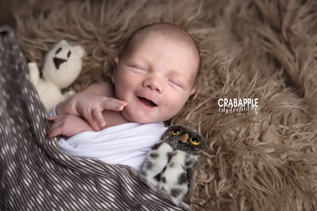 Brown Toned Newborn Baby Photoshoot Newborn baby sleepily smiling on brown fur with stuffed animals during a natural newborn baby photoshoot