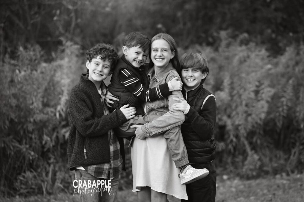 Black and white outdoor portrait of four siblings hugging
