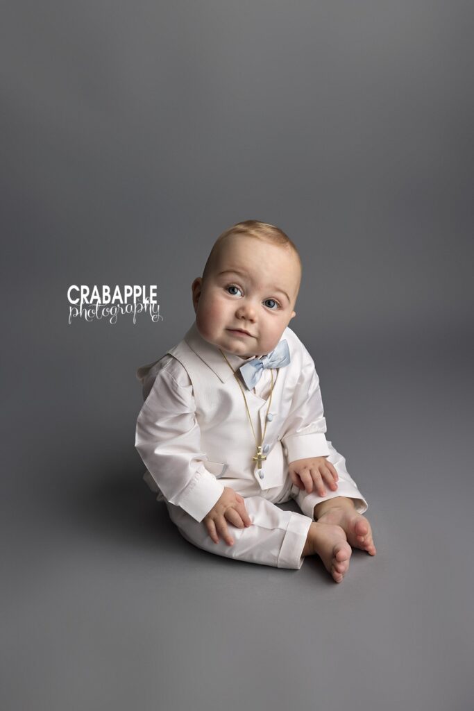 Baby boy in formal clothing sitting by himself in front of gray backdrop during 9 month sitter session photos