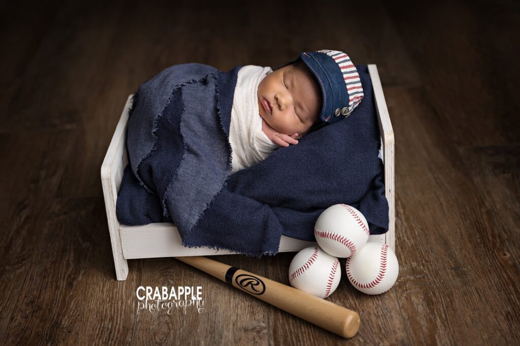 Newborn portrait with small white wooden bed, baseballs and bat for a personalized touch