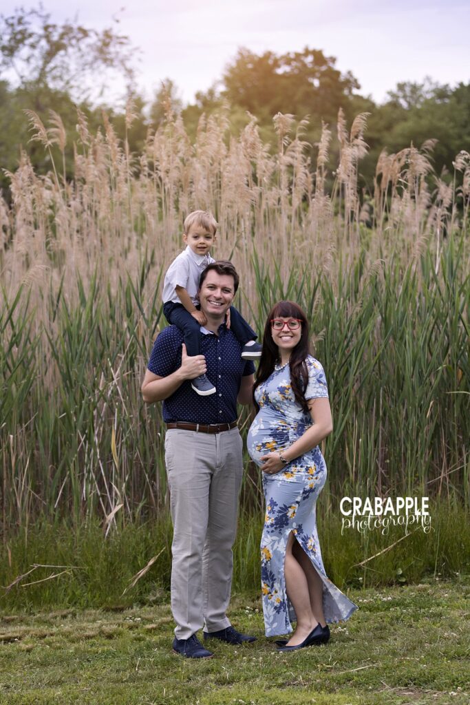 Family standing together in tall grass during an outdoor maternity photoshoot

