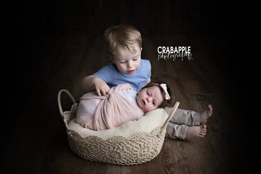 Natural newborn photography with toddler sibling beside baby using soft neutral tones in Ipswich MA

