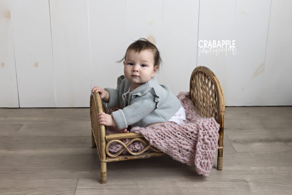 Photo of a 6 month old baby girl sitting unassisted in small bed prop during baby portrait session near Newton MA