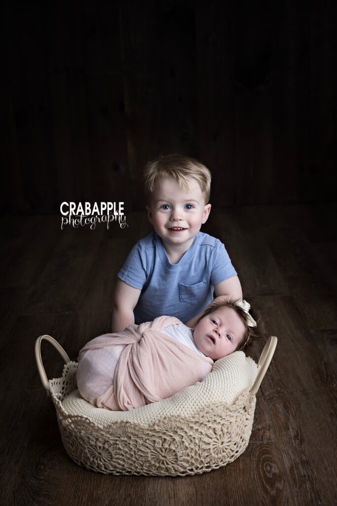 Studio newborn photography showing toddler brother with newborn baby in a calm, neutral setting
