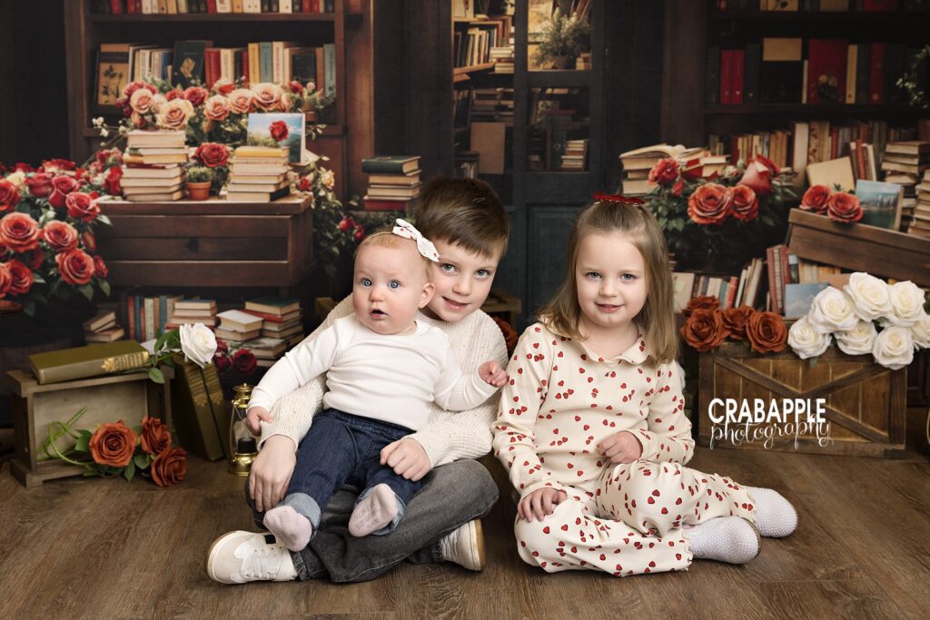 Siblings sitting together during Valentine’s Day mini sessions with a classic storybook backdrop