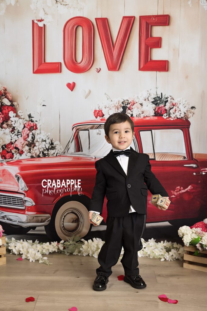 Child standing in front of a vintage red truck during a Valentine mini photo session