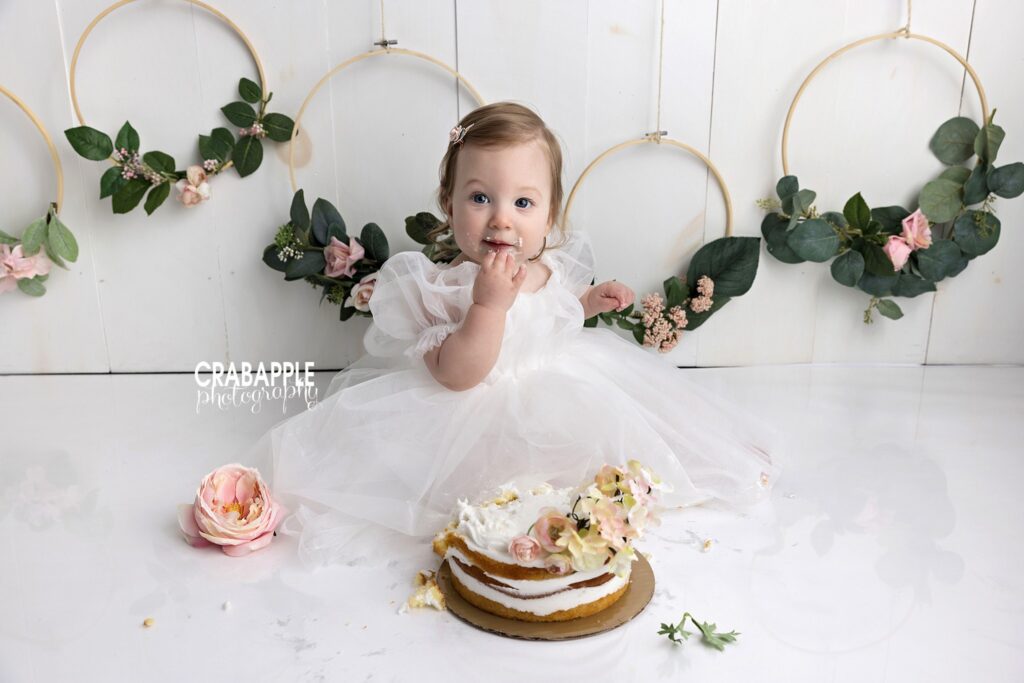 baby girl cake smash with light neutral backdrop and greenery
