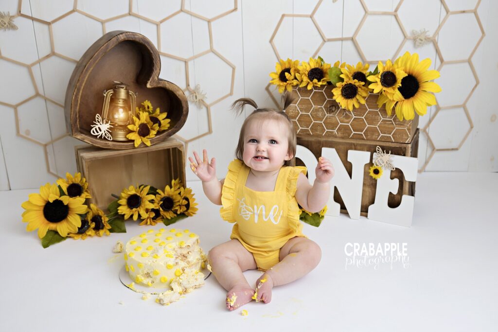 One-year-old baby smiling during a bright floral sunflower cake smash photoshoot in a Massachusetts studio
