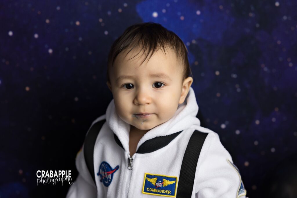one year old baby portrait in astronaut outfit against galaxy backdrop
