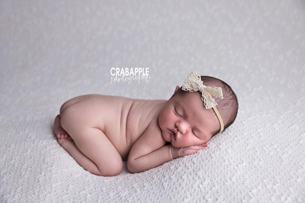 Neutral inspiration for newborn baby girl photos A neutral newborn baby girl photo with baby girl curled up on her tummy on a white blanket and wearing a cream colored headband