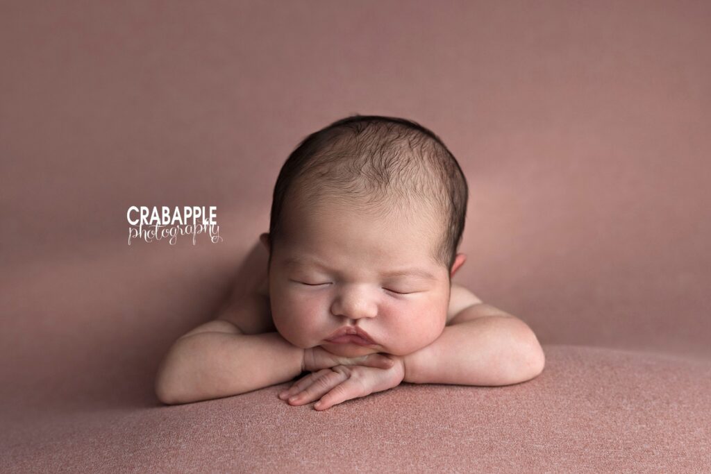 Baby Girl Newborn Photos Sleeping newborn baby girl with chin on hands in front of pink background during North Andover newborn photography session
