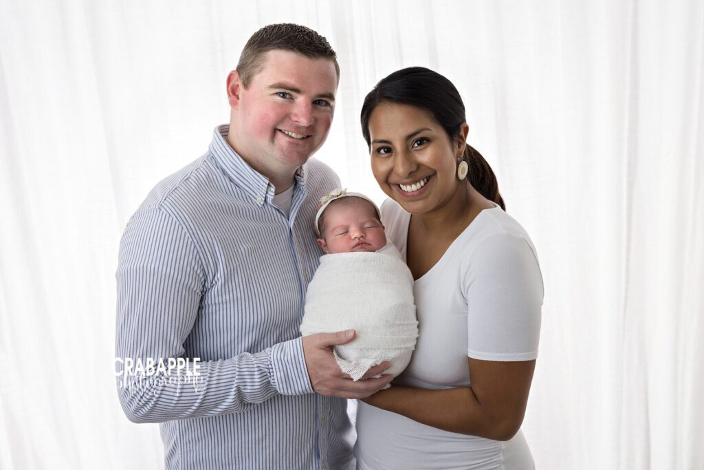Newborn Family Portraits Parents holding newborn baby girl during family photography session with white and pale blue styling