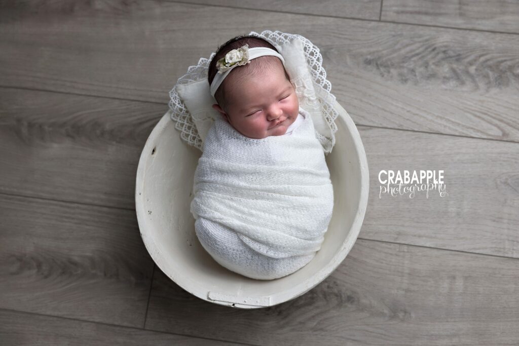 Newborn baby girl wrapped in white blanket posed in wooden bowl for timeless newborn photography wall art

