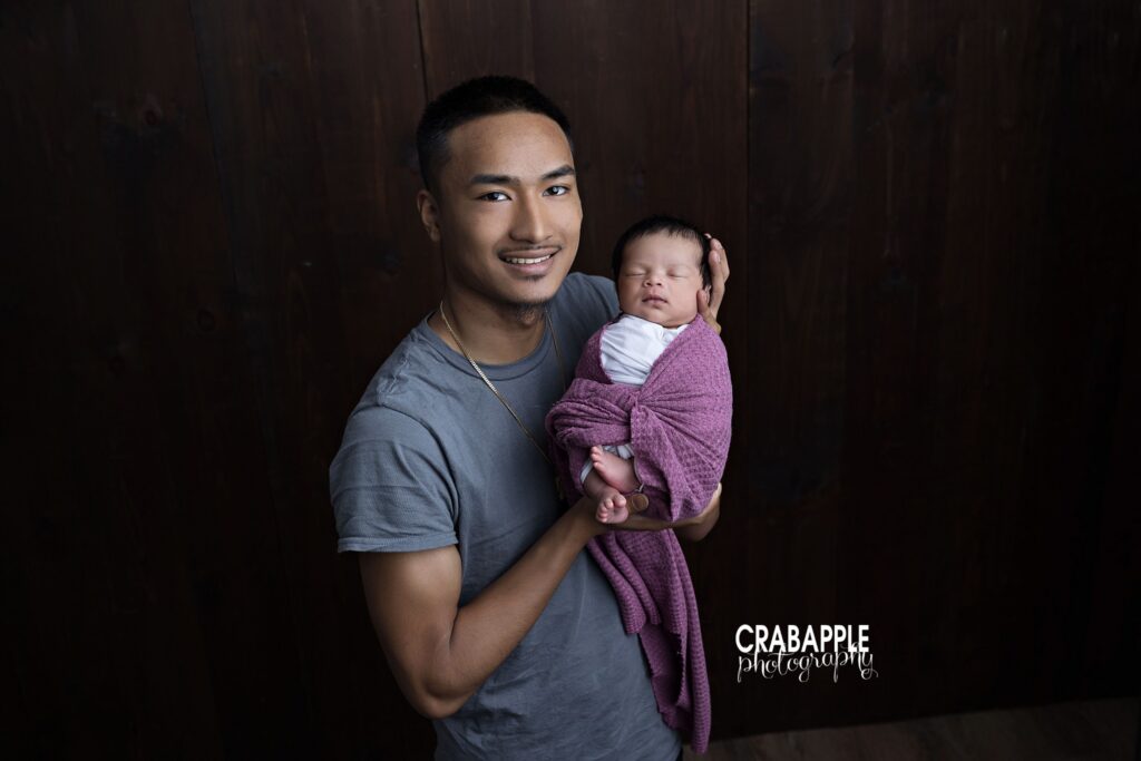 father holding newborn baby portrait simple background
