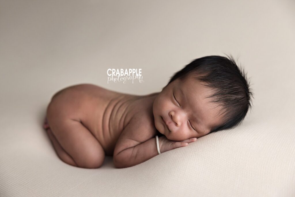 newborn posed on tummy with legs tucked under neutral backdrop
