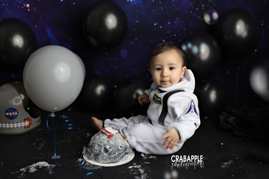 baby in astronaut outfit with space themed cake smash setup
