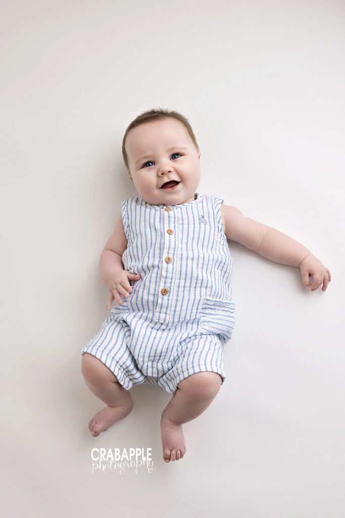 baby boy smiling during 8 month baby photoshoot in studio on white backdrop with blue and white striped outfit 8 month photo outfit ideas