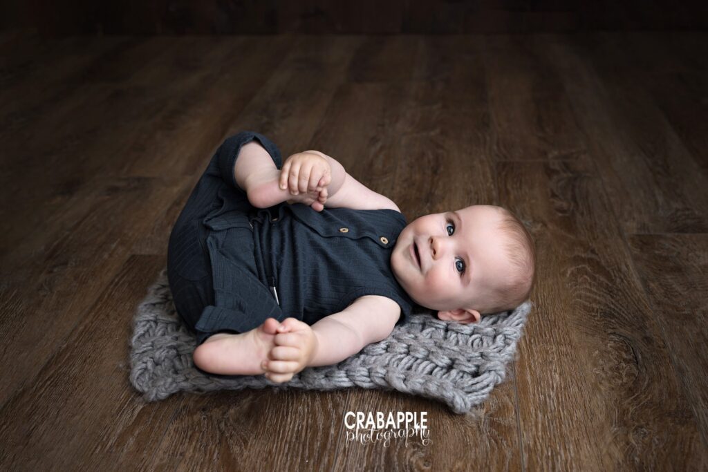 Knit blanket pose baby boy laying on chunky knit blanket and grabbing toes studio session