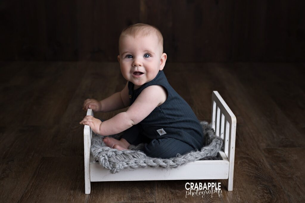 White bed prop baby boy sitting on small white wooden bed prop