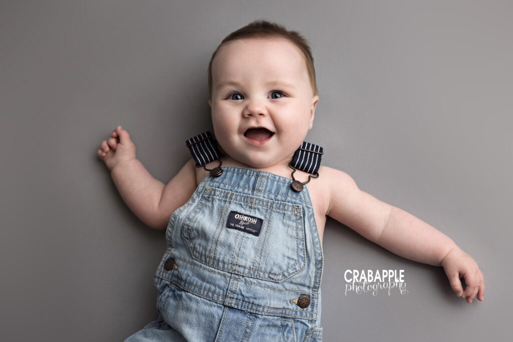Smiling baby boy in denim overalls with gray background 8 month photo outfit ideas