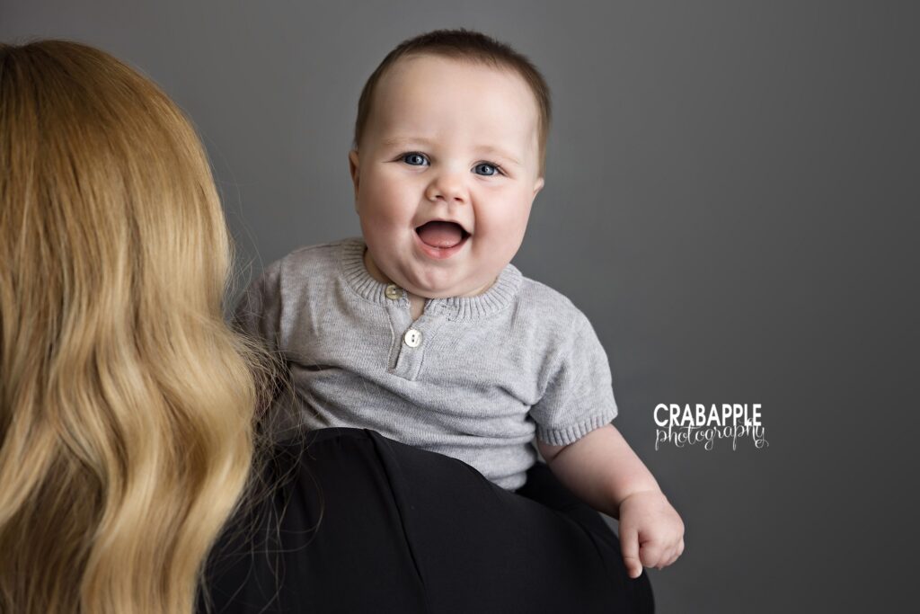 Happy baby smiling as he looks over mom's shoulder towards camera baby milestone photos Amesbury