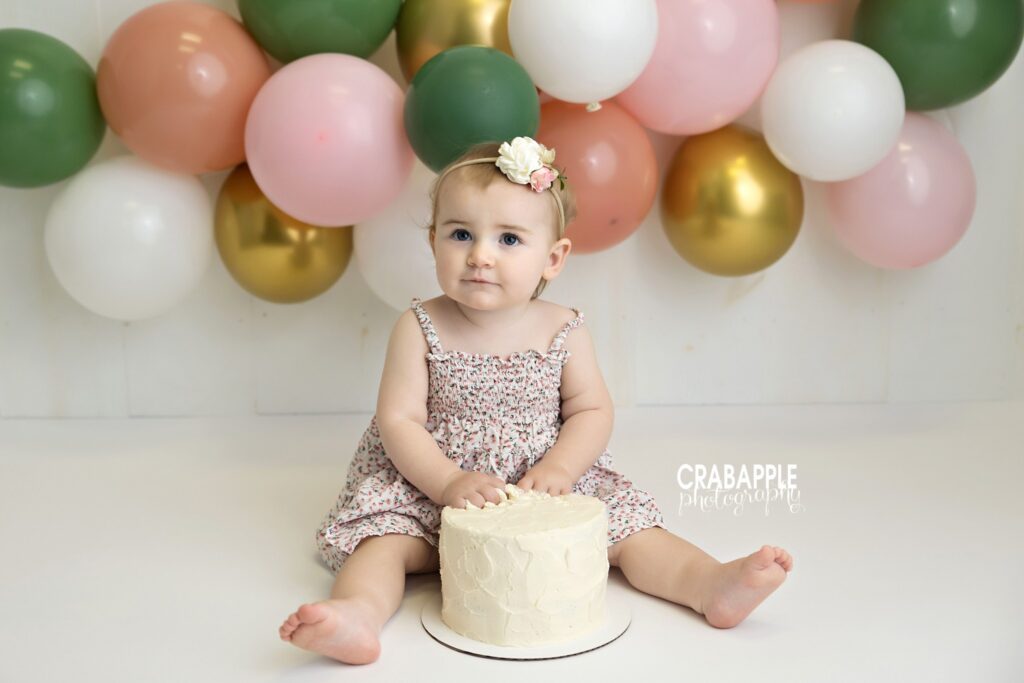 baby girl sitting clean cake smash setup with balloons
