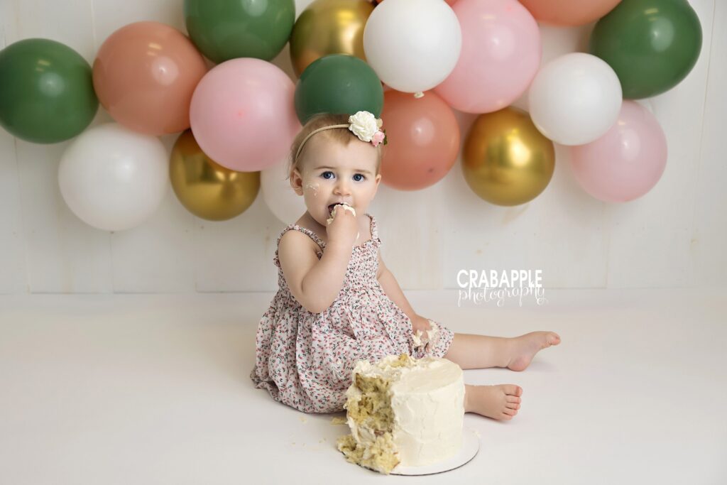 baby girl sitting surrounded by pastel balloons cake smash
 