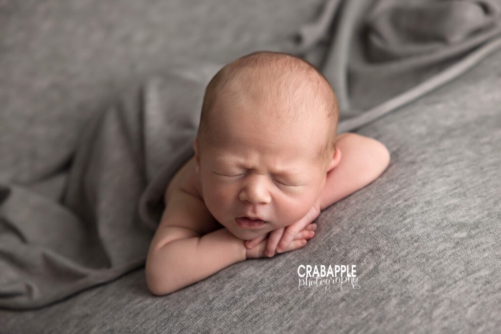 Sleeping newborn has chin resting on hands with gray cozy background during Andover MA newborn photographer session