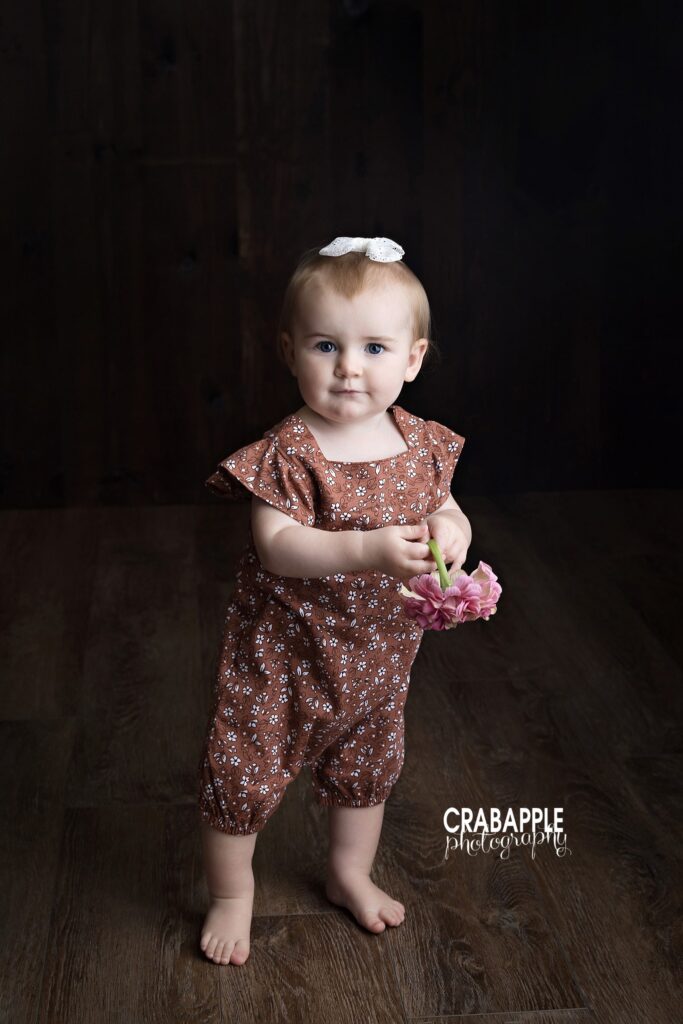 Baby girl standing at one year first birthday portrait session