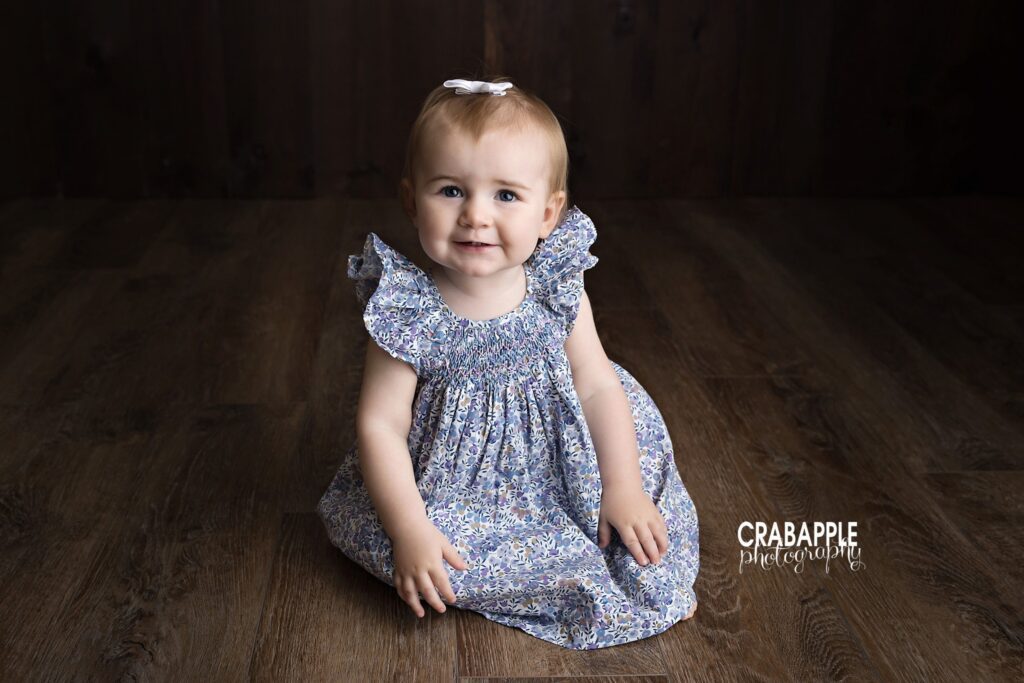 baby girl sitting in blue floral dress studio portrait for first birthday near Needham MA