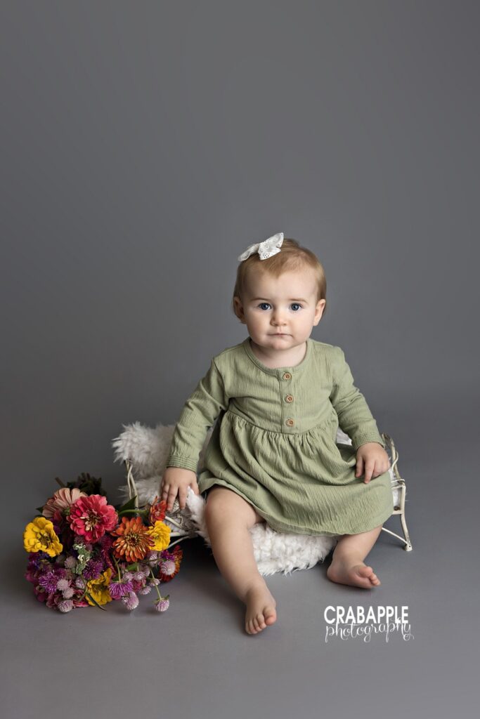 baby girl sitting on gray background with flowers and metal vintage bed prop