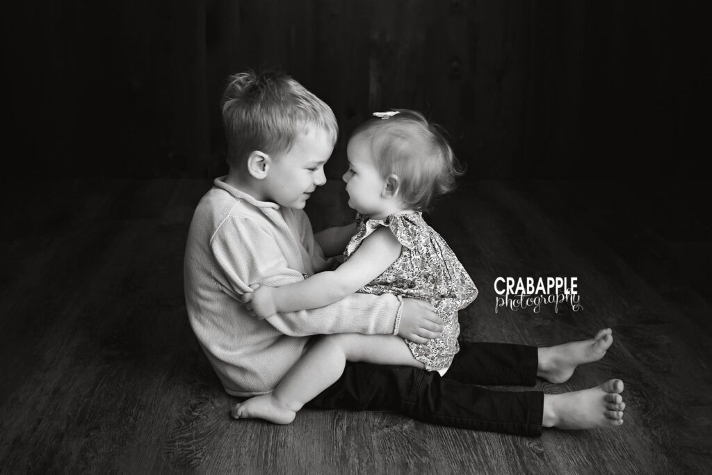 toddler boy holding baby sister during sibling photoshoot black and white portrait