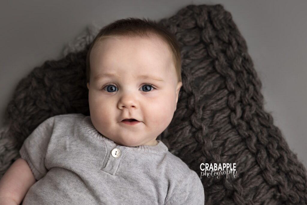 Close up solo portrait of baby boy with gray background and chunky knit blanket at baby photography studio near Amesbury