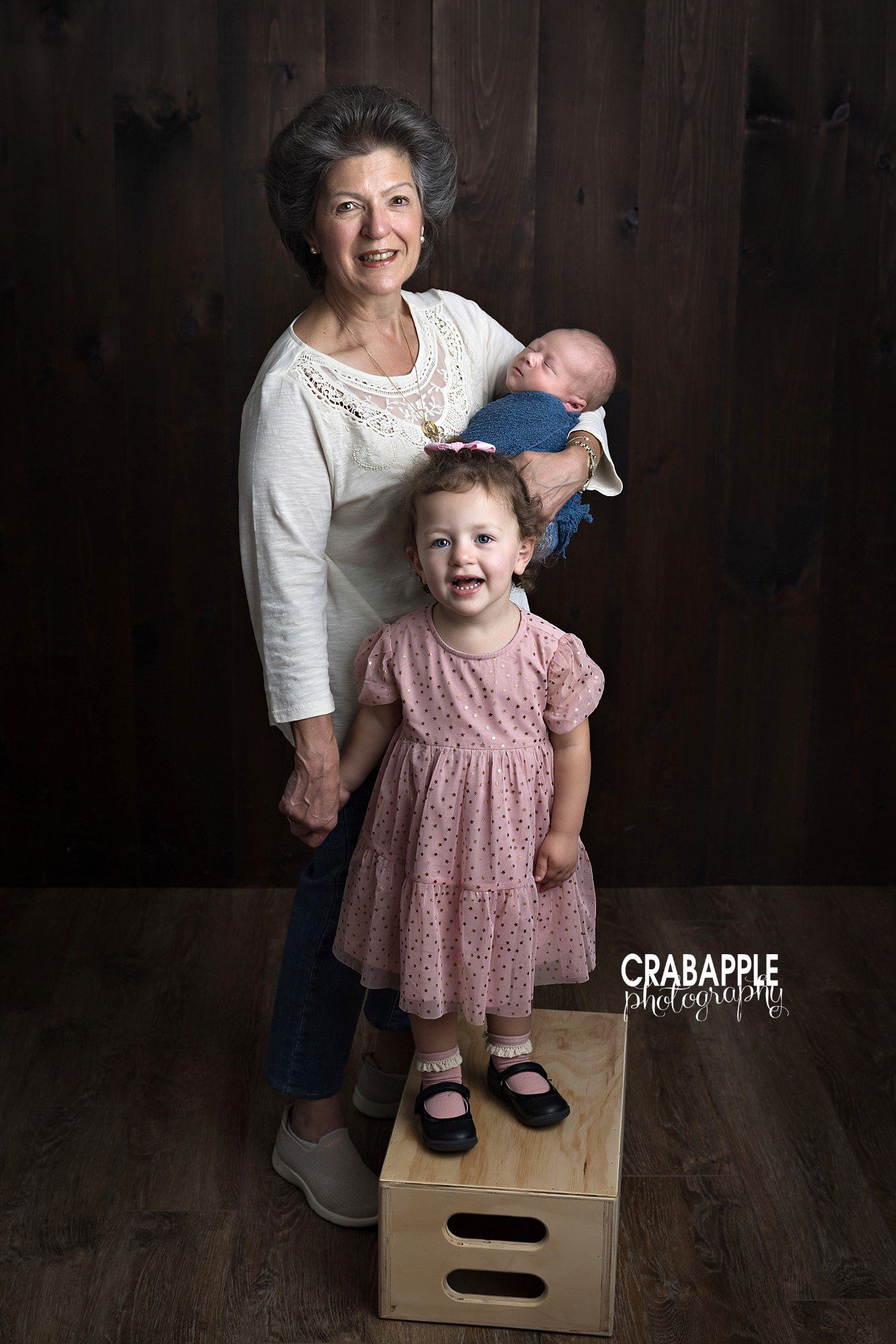 grandmother holding newborn baby boy in studio with toddler granddaughter
