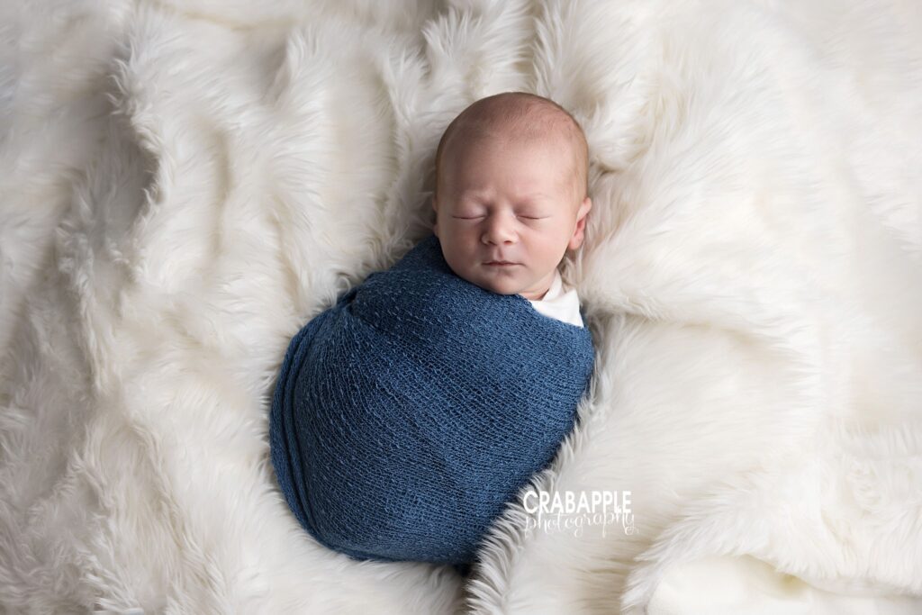swaddled newborn baby boy lying on soft cream blanket
