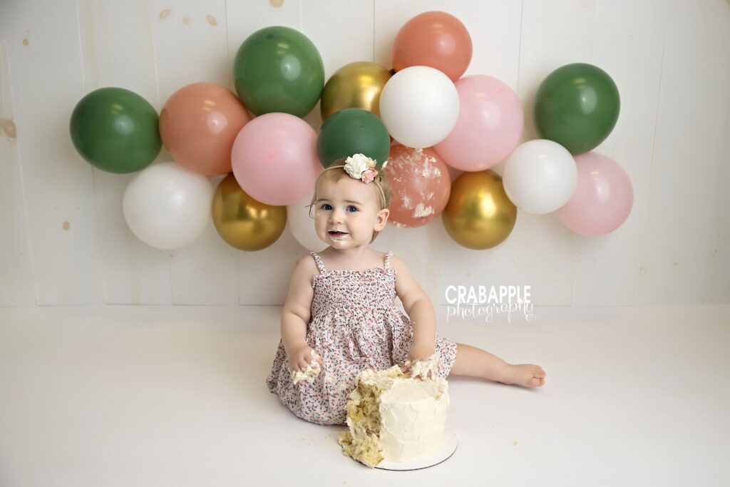 baby girl smiling with cake and balloons first birthday photoshoot
