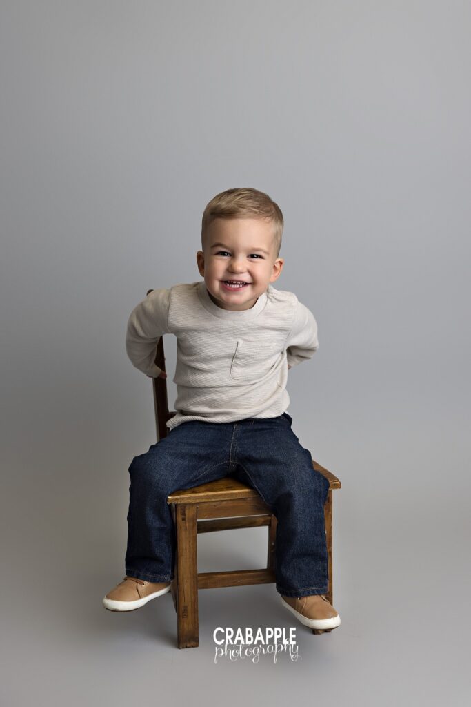 toddler smiling sitting on chair gray backdrop
