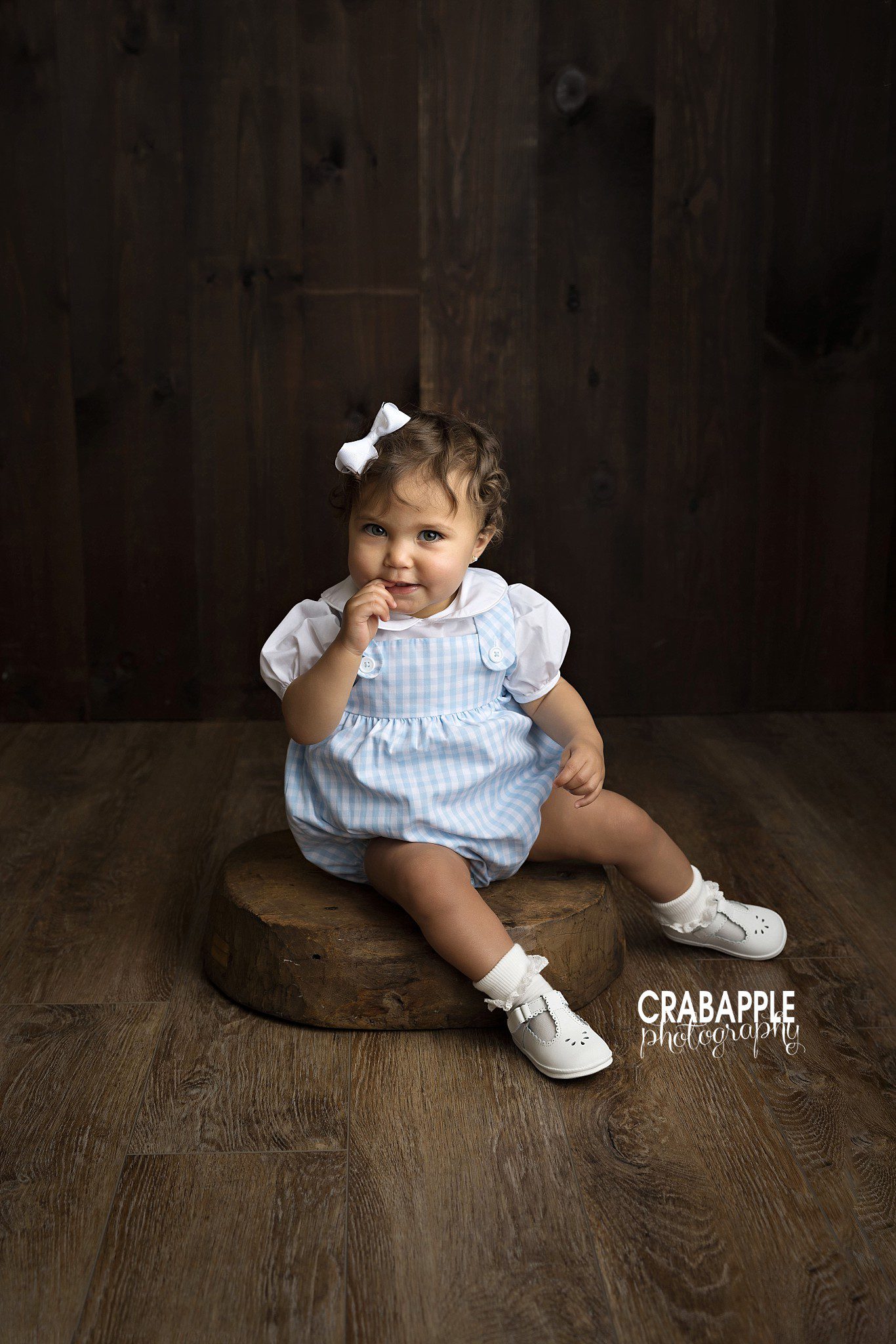 one year old baby girl sitting on wood floor portrait during first birthday photoshoot
